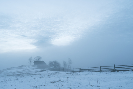 Landscape with a house on a hill in the village. Winter morning with a fogの写真素材