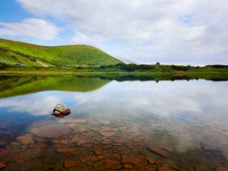 Summer landscape. Mountain lake with stones at the bottom. Hill with green grass. Sunny weather. Carpathians, Ukraine, Europeの写真素材