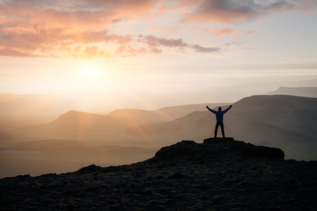 Adventure in the mountains of Iceland. Tourist is standing on a rock against the background of the setting sun. Location near Dyrholaey Cape in southern Icelandの写真素材