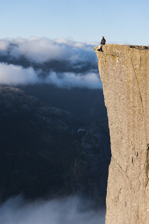 Norway, Forsand, rock formation Preikestolen, July 05, 2017: tourist guy sits on a cliff. Tourist attraction towers over the Lysefjordのeditorial素材