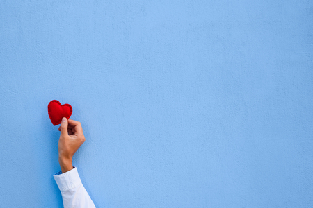 Red Valentine heart in a man's hand on blue wall background. Greeting card with copy space for textの写真素材