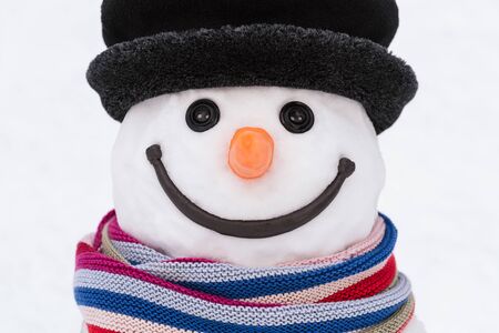 Portrait of a smiling snowman with a striped scarf and a black hat. Button eyes and carrot noseの写真素材