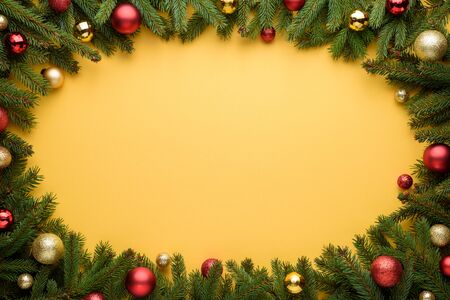 Oval frame of Christmas balls and fir branches. Yellow background for Christmas and New Year design. Copy space for promotions, advertising and congratulation textの写真素材