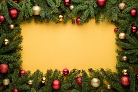Decorative frame of Christmas balls and fir branches. Yellow background for Christmas and New Year design. Copy space for promotions, advertising and congratulation textの写真素材