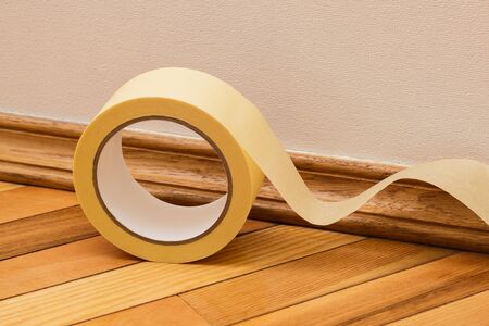 Preparing a room for painting walls. Masking the baseboard with a yellow masking tape. Repair in the...