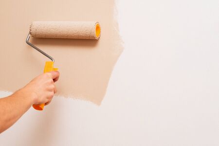 Repair in the house. A man paints the walls with a roller in beige. Concept with copy space for textの写真素材