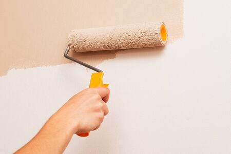 Repair in the house. A man paints the walls with a roller in beige colorの写真素材