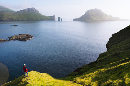 Tourist Hiking in the Faroe Islands along the old postal route to Gasadalur with views of Drangarnir and Tindholmurの写真素材