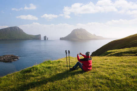 Tourist photographs the view of the Drangarnir sea stacks and the Tindholmur islet. The old postal route to Gasadalur, Faroe Islandsの写真素材