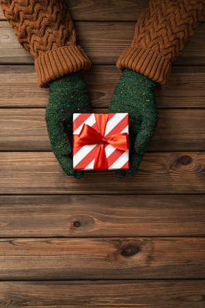 Christmas card with present in the hands of a woman on wooden background with copy space for textの写真素材