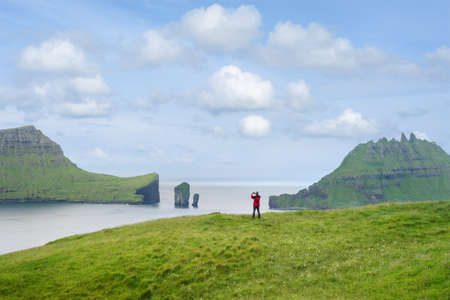 A tourist photographs a view of Drangarnir sea stacks and the Tindholmur isletの写真素材