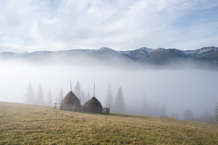 Autumn landscape with calm peaceful countryside view with morning mist, haystacks and mountain peaksの写真素材