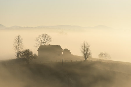 Peaceful view of a house in the morning autumn fog on a hill in a mountain villageの写真素材