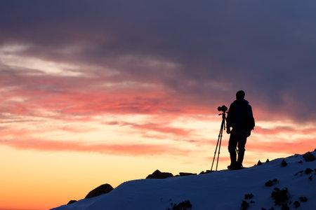 Landscape photographer with a tripod shooting in the mountains at sunsetの写真素材