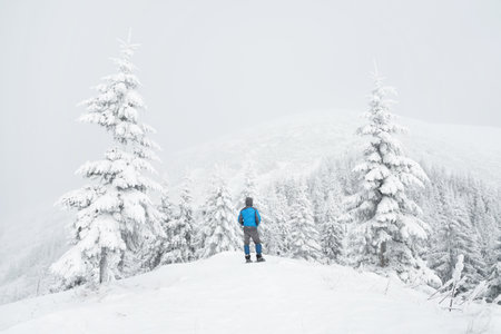 A man stands on a hill in a snow-covered mountain forest in winterの写真素材