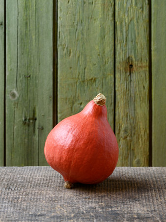 Red Kuri or Uchiki Kuri Squash or Hokkaido Pumpkin on an Old Wooden Table with Green Background and Copy Spaceの写真素材