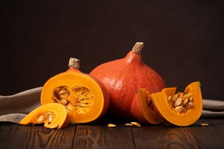 Hokkaido Pumpkins or Red Kuri Winter Squash on a Wooden Table with One Cut into Slicesの写真素材