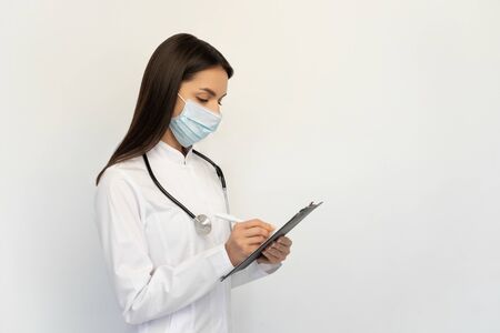 Friendly female doctor in a protective medical mask with a stethoscope, concept of protection against covid-19の写真素材