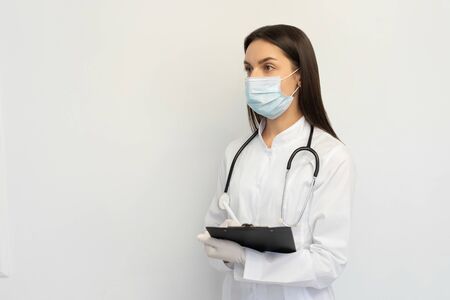 Female doctor in a protective medical mask and gloves, writes the diagnosis to the clients cardの写真素材