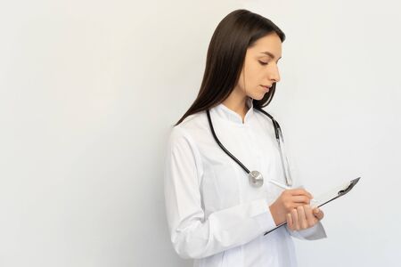 Friendly female doctor, writes the diagnosis to the clients card, a stethoscope on his neckの写真素材