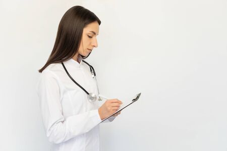 Friendly female doctor, writes the diagnosis to the clients card, a stethoscope on his neckの写真素材