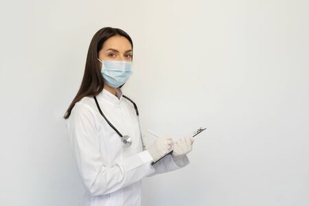 Female doctor in a protective medical mask and gloves, writes the diagnosis to the clients cardの写真素材