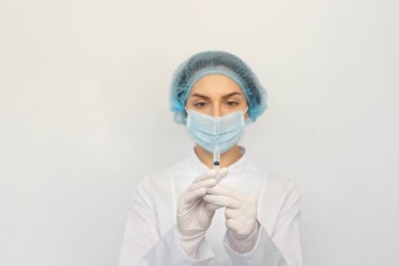 Female doctor in a protective medical mask and gloves with a syringeの写真素材
