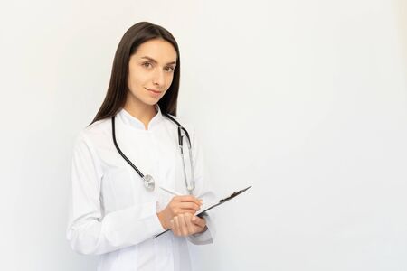 Friendly female doctor, writes the diagnosis to the clients card, a stethoscope on his neckの写真素材
