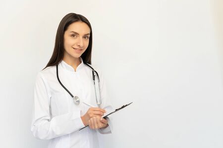 Friendly female doctor, writes the diagnosis to the clients card, a stethoscope on his neckの写真素材