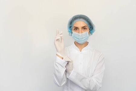 A female doctor in a medical mask puts white rubber glovesの写真素材