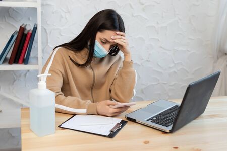 woman girl wearing a protective mask sits at a table, with a high fever and headache, works with a...