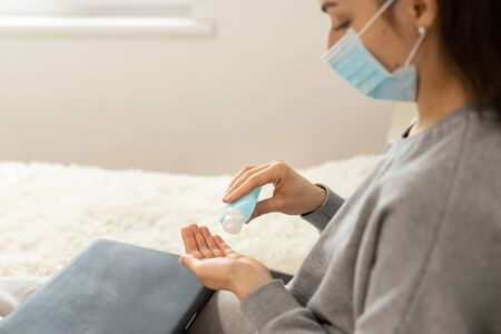 Coronavirus. Business woman working from home wearing protective mask. Business woman in quarantine for coronavirus wearing protective mask. Working from home. Cleaning her hands with sanitizer gel.の写真素材
