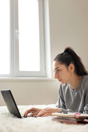 Young girl woman on the bed, distance learning for students. Coronavirus. Quarantine. Woman look at a laptop computer. Freelancer, distant work, work at home, online educationの写真素材