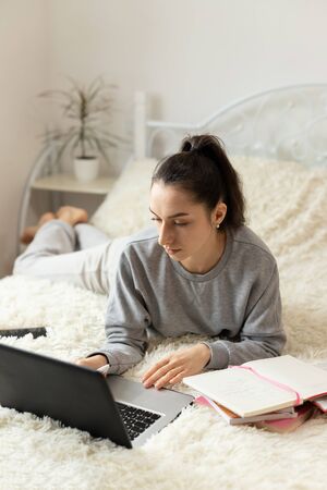 Young girl woman on the bed, distance learning for students. Coronavirus. Quarantine. Woman look at a laptop computer. Freelancer, distant work, work at home, online educationの写真素材