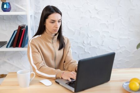 Young girl woman sits at a table, distance learning for students. Quarantine, self-isolation. Woman look at a laptop computer. Freelancer, distant work, work at home, online educationの写真素材