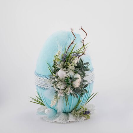 handmade decorative Easter turquoise egg on a white background with ornaments textile and flowersの写真素材