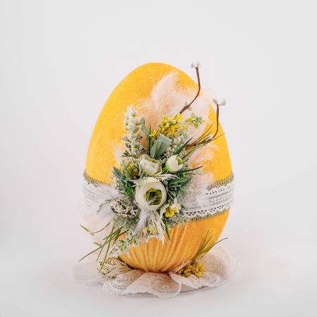 handmade decorative Easter yellow egg on a white background with ornaments textile and flowersの写真素材
