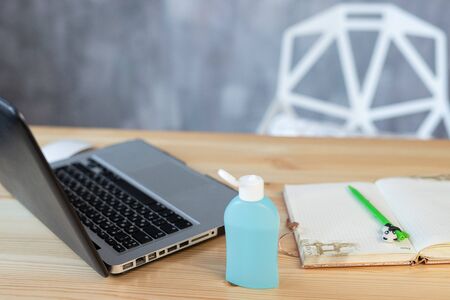 Medical protective mask and hand sanitizer in a bottle, laptop pen notebook lies on a wooden table, working online or learning in quarantine, epidemic coronavirus covid-19の写真素材