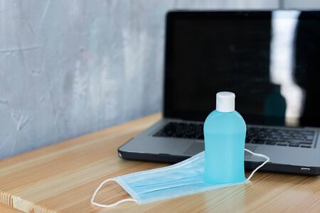 Medical protective mask and hand sanitizer in a bottle on a laptop background, working online or...