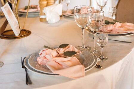 Festive table setting with empty wineglasses. Selebration banquet with pink napkins, white plates and wineglasses for white and red wine on the white table in restaurantの写真素材