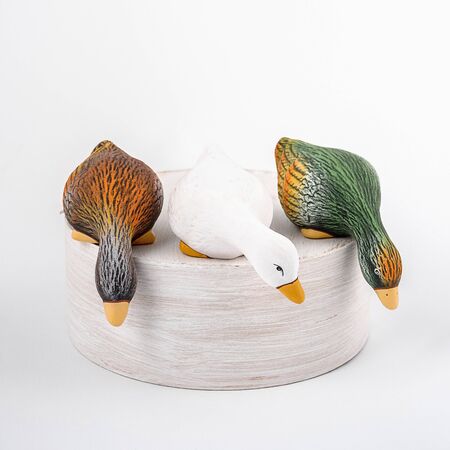 Three ceramic ducks stay on stump and look down. Isolated colorful ducks for gardenの写真素材