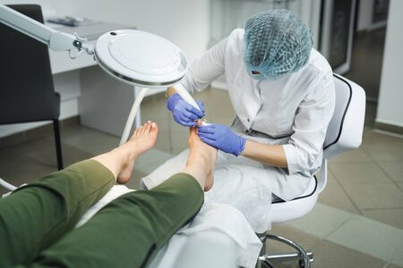 Podologist with special electric equipment for caring about foot and nails. Professional hardware pedicure using electric machine in SPA salonの写真素材