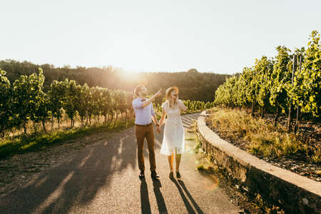 Stylish couple walking among vineyard and they surprised by what they saw. Girl in white dress holds hand of manの写真素材
