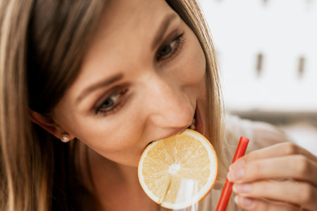 Close-up portrait of a beautiful young woman drinking orange juice in the cafeの写真素材
