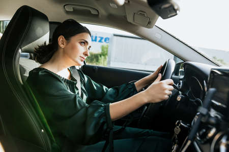 Serious brunette woman driving car. Young woman in green salon of car look away forward