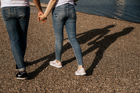 Close up of romantic couple hold hands and walk along the shore. Focus on the feet and hands of...