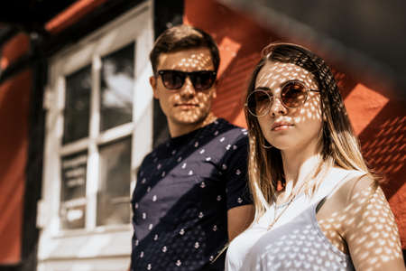 Close up of romantic couple stand and look in camera with shadow of sunlight. Serious man and woman on building backgroundの写真素材