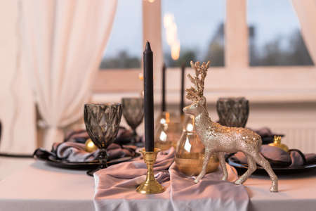 Close up of festive Christmas table setting with empty wine glasses and black plate with gold deer. Concept of Christmas and New Yearの写真素材