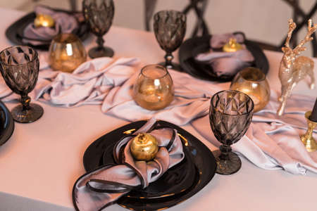 Close up of festive Christmas table setting with empty wine glasses and black plate with gold...