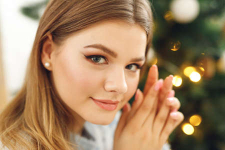 Portrait of girl wears festive clothes at home near Christmas Tree. Happy woman sit in blue sweater with deer and gray stockingsの写真素材